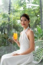 Portrait of a beautiful woman holding a glass of orange juice looking at you sitting at home Royalty Free Stock Photo