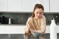 Portrait of beautiful woman at home, eating her breakfast, holding spoon, leaning on worktop and having cereals with Royalty Free Stock Photo