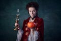 Portrait of beautiful woman in image of vampire holding candle and pumpkin  over dark green background. Trick or Royalty Free Stock Photo