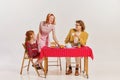 Portrait of beautiful woman, man and little girl sitting at the table and having breakfast isolated over grey background Royalty Free Stock Photo