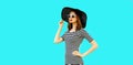 Portrait of beautiful woman model looking away wearing black round summer hat, striped dress isolated on blue background Royalty Free Stock Photo
