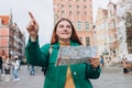 Portrait beautiful woman with paper map in street. Happy tourist travels in Europe. Redhead girl with backpack pointing Royalty Free Stock Photo