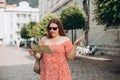 Portrait beautiful woman with paper map on urban street. Young worried female traveler lost in the city using map