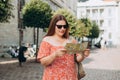 Portrait beautiful woman with paper map on urban street. Young worried female traveler lost in the city using map