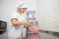 Portrait of beautiful woman pastry chef, wearing white hat and apron, mixing the flour in a pink bowl using a whisk Royalty Free Stock Photo