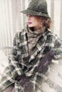 Portrait of a beautiful woman in profile in a retro hat and plaid coat on a bench in winter in a snowfall