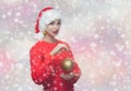 Portrait of a beautiful woman in a red Santa Claus hat and knitted red sweater holding a golden christmas ball Royalty Free Stock Photo