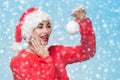 Portrait of a beautiful woman in a red Santa Claus hat and knitted red sweater holding a white christmas ball on snowflakes backg Royalty Free Stock Photo