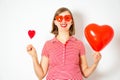 Portrait of beautiful woman in red sunglasses holding in her hands red heart balloon and lollipop. Royalty Free Stock Photo