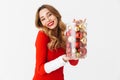 Portrait of beautiful woman 20s wearing Santa Claus red costume smiling and holding Christmas tree decorations, isolated over Royalty Free Stock Photo