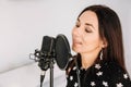 Portrait of beautiful woman sings a song near a microphone in a recording studio. Place for text or advertising