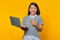 Portrait of beautiful woman smiling while pointing at laptop on yellow background
