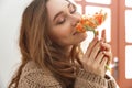 Portrait of beautiful woman in sweater with long brown hair sitting at table in coffee shop, and smelling flower Royalty Free Stock Photo