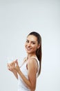 Portrait of beautiful woman taking vitamin pill with glass of fresh water indoors. Smiling girl taking omega 3 fish oil capsule Royalty Free Stock Photo