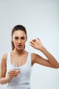 Portrait of beautiful woman taking vitamin pill with glass of fresh water indoors. Smiling girl taking omega 3 fish oil capsule Royalty Free Stock Photo