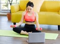 Portrait of beautiful woman wearing a sport suit sitting on a yoga mat holding a dumbbell doing exercise by following the Royalty Free Stock Photo