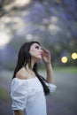 Portrait of beautiful woman in white dress standing in street surrounded by purple Jacaranda trees Royalty Free Stock Photo