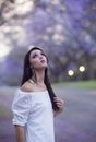 Portrait of beautiful woman in white dress standing in street surrounded by purple Jacaranda trees Royalty Free Stock Photo