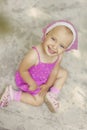 Portrait of beautiful 3 years old girl in pink summer dress and pink kerchief. Child sits on ground and looks in camera. View of Royalty Free Stock Photo