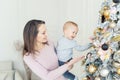 Portrait of beautiful young adult caucasian woman with cute adorable little blond toddler boy enjoy trimming christmas tree in Royalty Free Stock Photo