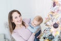 Portrait of beautiful young adult caucasian woman wiht cute adorable little blond toddler boy enjoy trimming christmas tree in Royalty Free Stock Photo