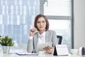 Portrait of beautiful young Asian business woman sitting and using a tablet behind the table in workplace Royalty Free Stock Photo
