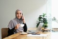 Portrait beautiful young asian muslim woman talking on mobile phone and using laptop at office Royalty Free Stock Photo