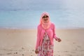 Portrait of beautiful young Asian muslim woman wearing pink dress and hijab standing by tropical beach looking at camera Royalty Free Stock Photo