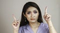 Portrait of beautiful young Asian woman confuse and pointing fingers upward at copy space isolated over white background