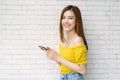 Portrait of beautiful young Asian woman wear yellow off-shoulders clothes holding smartphone, standing and looking at camera white Royalty Free Stock Photo