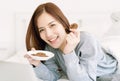 Portrait of beautiful young Asian woman wearing sweater eating cookie in bed at home bedroom, looking at camera. Relax and Royalty Free Stock Photo