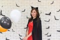 Portrait of beautiful young asian woman wearing witch costume posing with balloons on background decorated for party concept - Royalty Free Stock Photo