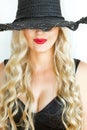 Portrait. Beautiful young blond woman in black hat with neckline on a white background smiles mysteriously. Royalty Free Stock Photo