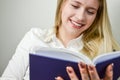 Portrait of a beautiful young blond woman smiling while reading a book Royalty Free Stock Photo