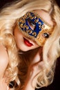 Portrait of a beautiful young blond woman with theatrical mask on his face on a dark background