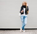 Portrait of a beautiful young blonde girl with long hair posing on a street with coffee and a backpack. Outdoor, warm color.