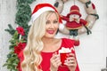 Portrait. A beautiful young blonde girl in a Santa`s cap is standing at the front door, decorated with a wreath and fir branches Royalty Free Stock Photo