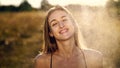 Portrait of a beautiful young blonde girl, under light summer rain, in the sun rays, on a green meadow. The girl smiles Royalty Free Stock Photo