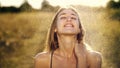 Portrait of a beautiful young blonde girl, under light summer rain, in the sun rays, on a green meadow. The girl smiles Royalty Free Stock Photo