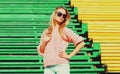 Portrait of beautiful young blonde woman sitting on bench wearing sunglasses, sweater in the city park Royalty Free Stock Photo