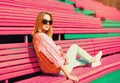 Portrait of beautiful young blonde woman sitting on bench wearing sunglasses, sweater in the city park Royalty Free Stock Photo