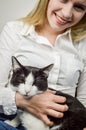 Portrait of a beautiful young blonde woman smiling while holding a black and white cat looking bored Royalty Free Stock Photo