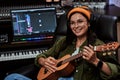 Portrait of beautiful young brunette, female artist sitting in recording studio and playing ukulele Royalty Free Stock Photo