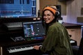 Portrait of beautiful young brunette, female artist smiling at camera while playing keyboard synthesizer, sitting in Royalty Free Stock Photo