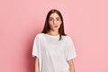 Portrait of beautiful, young , brunette girl posing in white t-shirt with grimacing face against pink studio background Royalty Free Stock Photo