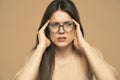 Portrait of beautiful young brunette with glasses touching her temples feeling stress, on beige background Royalty Free Stock Photo