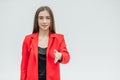 Portrait of a beautiful young brunette. Stretches your hand in congratulations. Dressed in a red jacket. Gray background