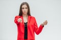 Portrait of a beautiful young brunette. Stretches your hand in congratulations. Dressed in a red jacket. Gray background