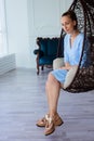 Portrait of beautiful young brunette woman in blue dress with make up and ponytail, sitting in large chair