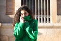Portrait of beautiful young brunette woman with curly hair and green woollen coat covering her face with the collar of the coat